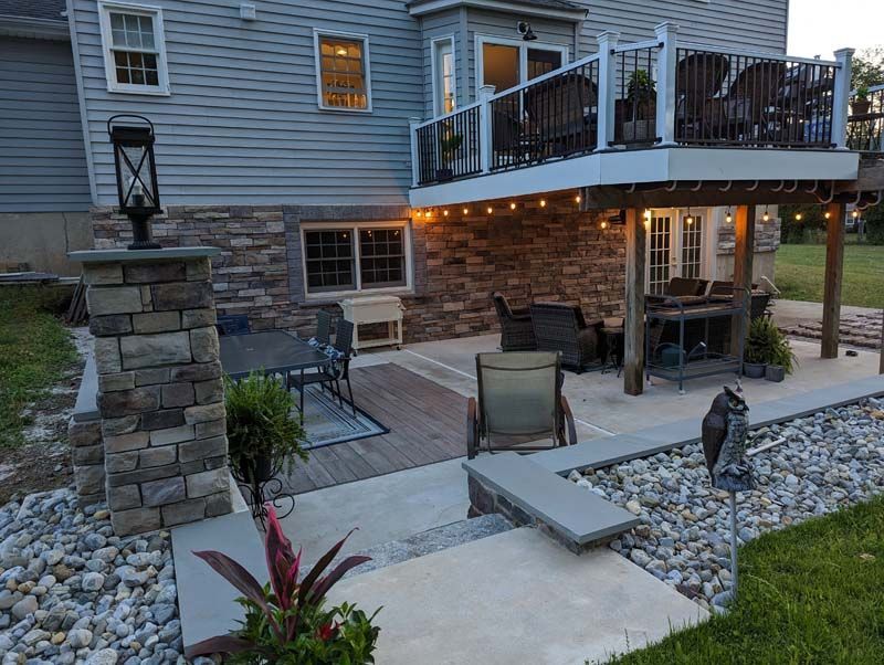 Backyard patio with deck, stone pillars, and string lights. Outdoor furniture and landscaping.
