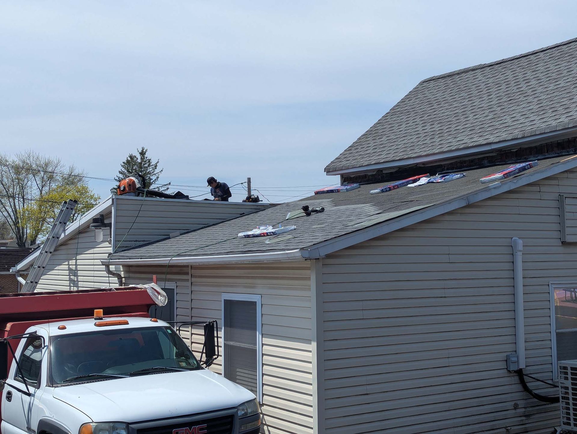 Roofers working on a house roof. White truck in foreground. Blue sky.