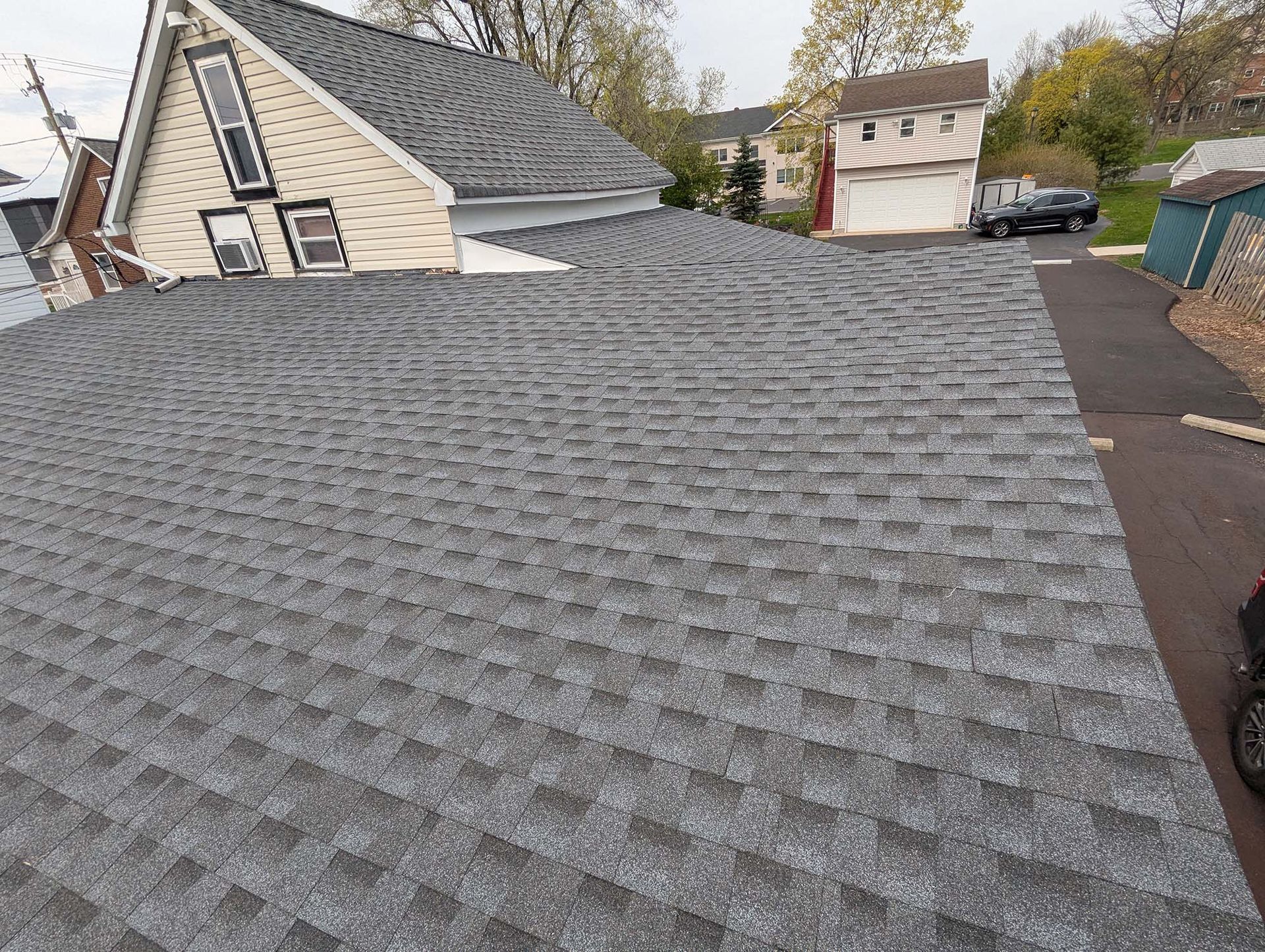 Gray asphalt shingle roof on a house, with a cloudy sky and other houses in the background.