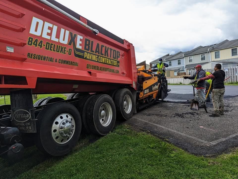 Red Deluxe Blacktop truck paving a road with workers directing the process.
