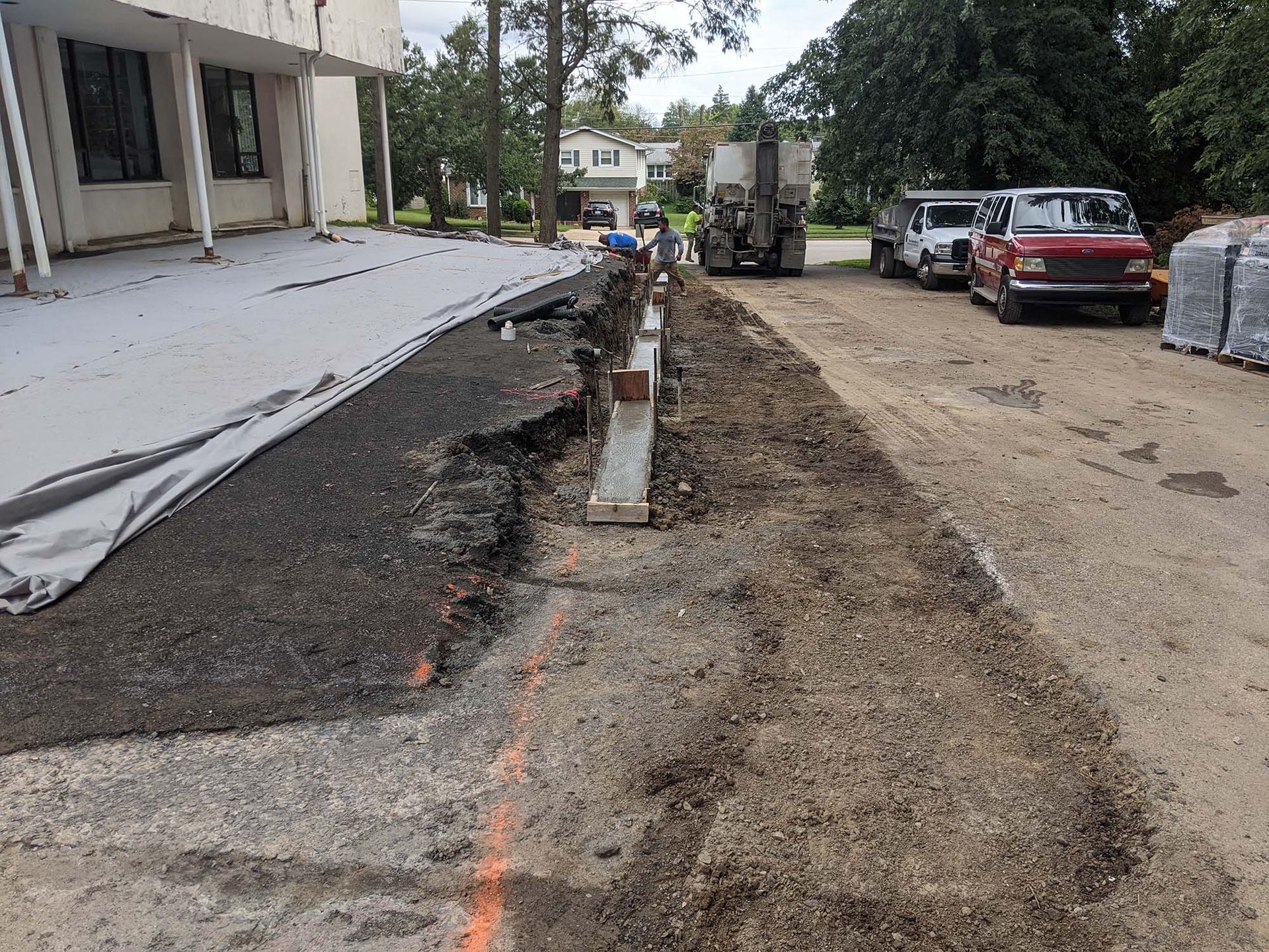 Road construction outside a building: asphalt removal, workers, trucks, and materials.