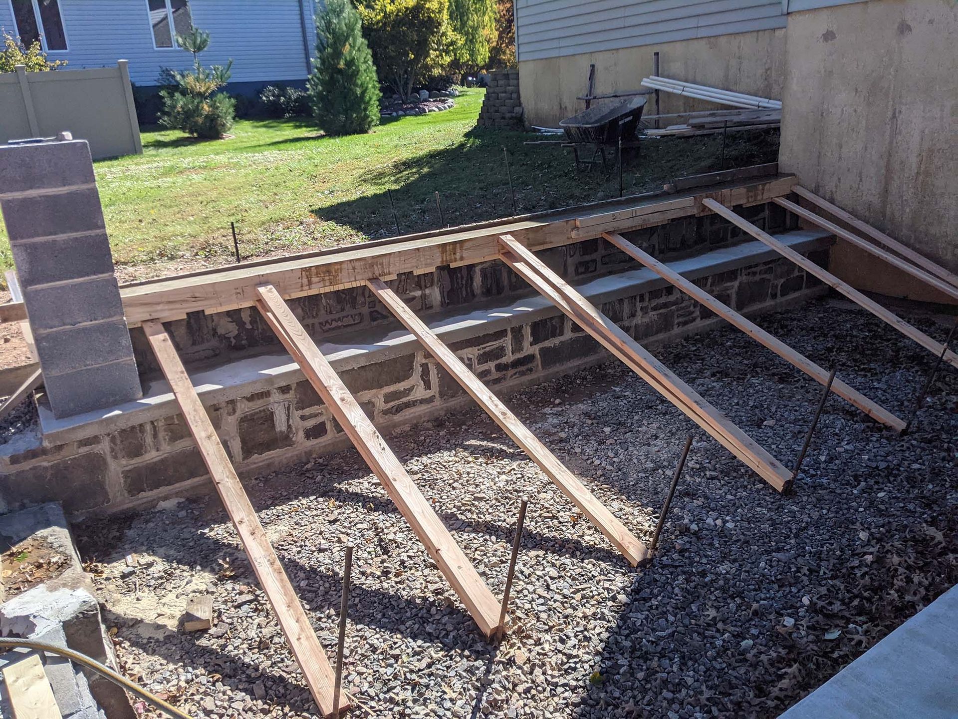 Construction of a small concrete and block retaining wall; wooden supports and gravel base visible.
