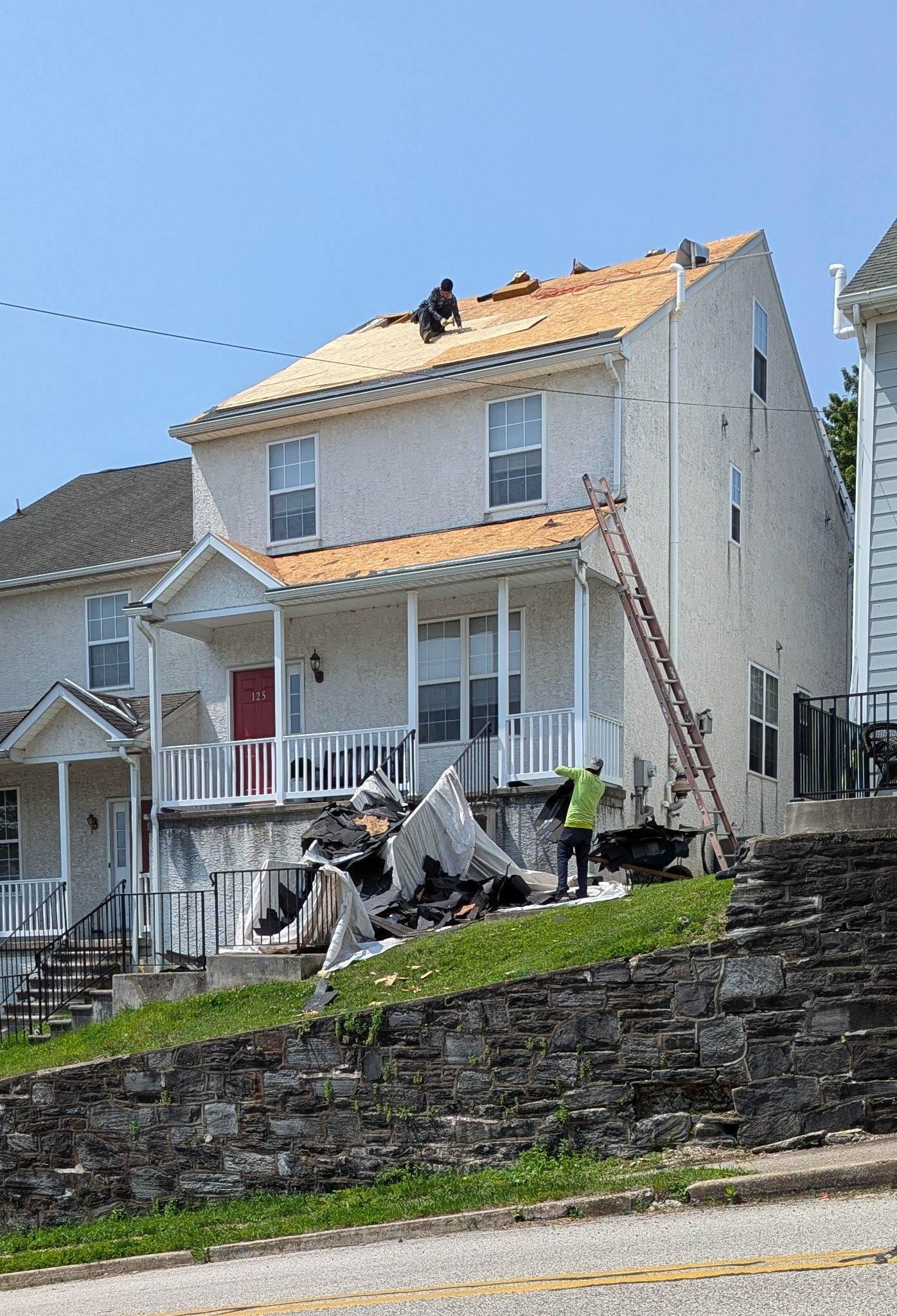 House undergoing roof repair; workers on roof and ground, ladder present, sunny day.