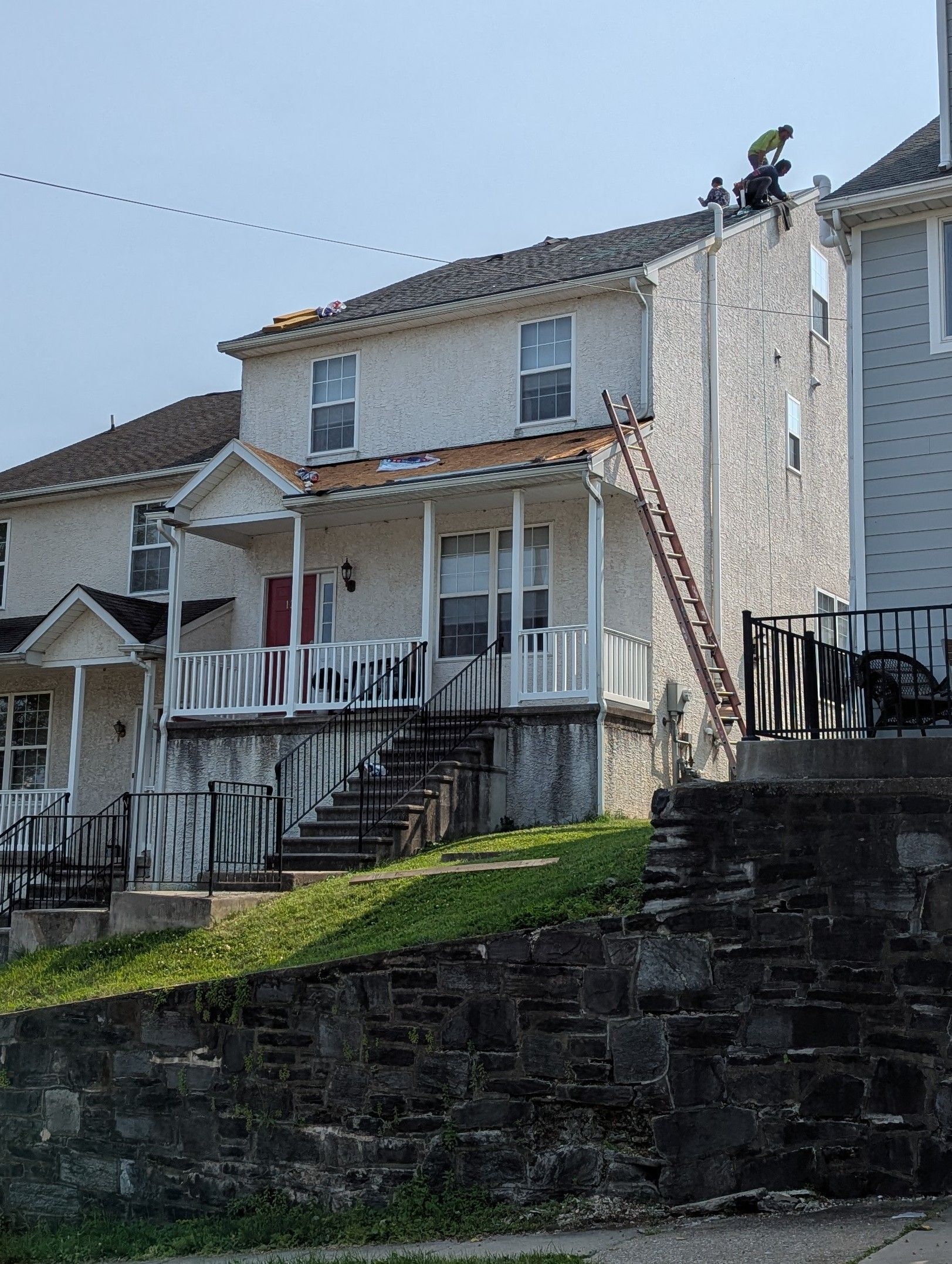 A two-story building with a ladder leading to a person working on the roof.