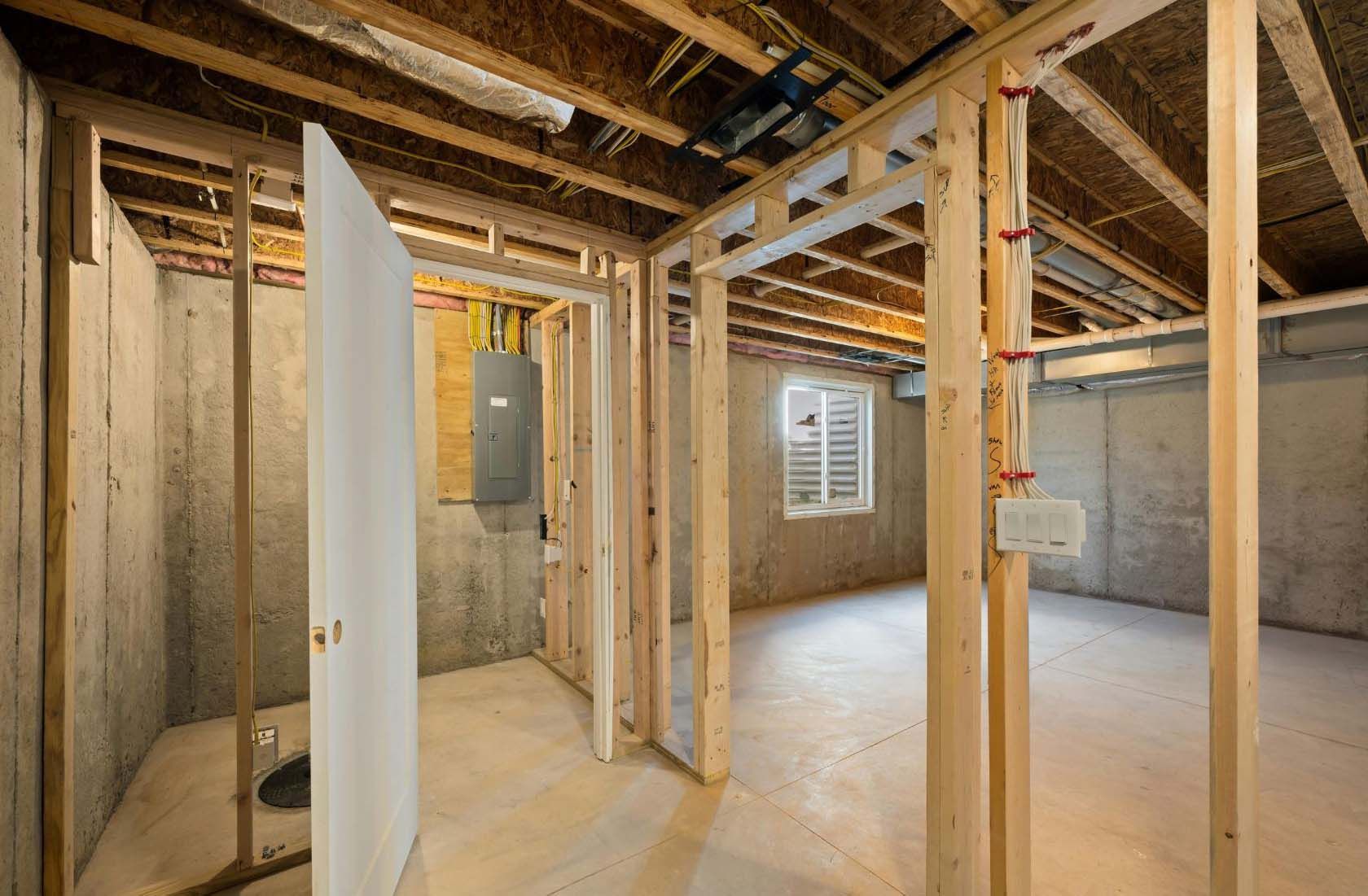 Basement room under construction, with wooden framing, unfinished walls, and exposed ceiling.
