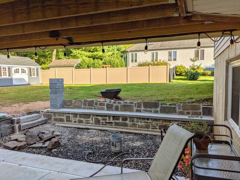 Patio with seating, stone wall, grassy yard, string lights, and a fire pit under wooden deck.