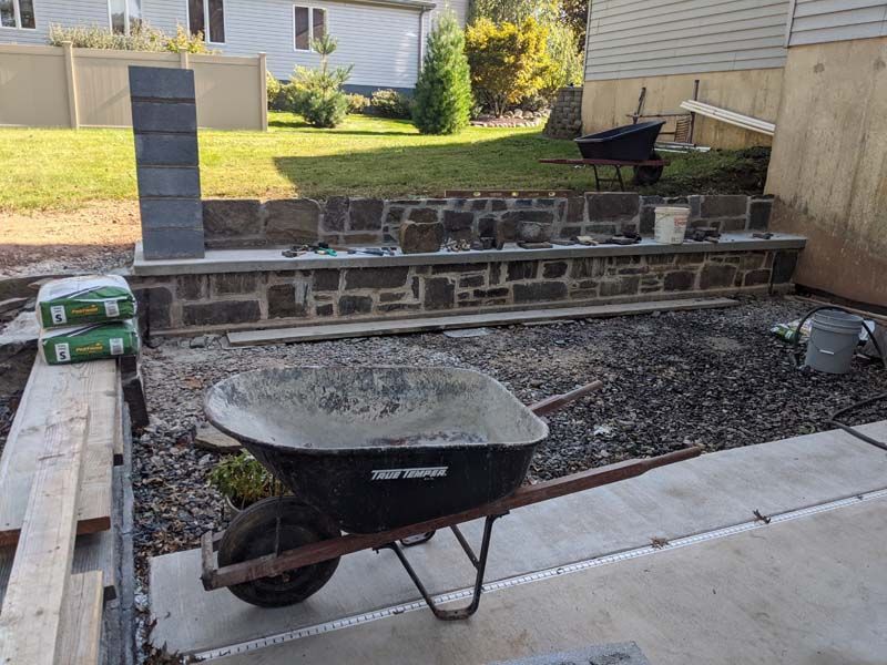 Construction site with a stone retaining wall, wheelbarrow, and cement bags.