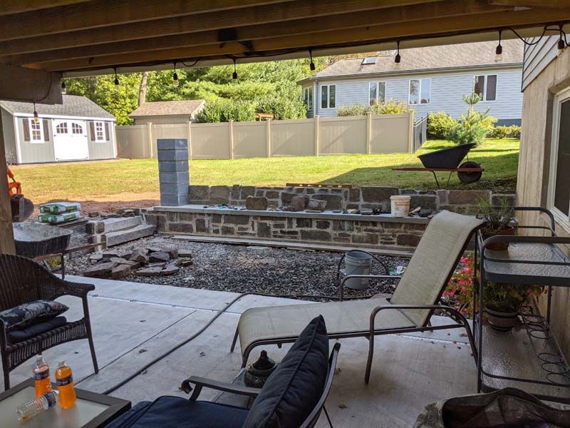 Backyard patio with lounge chairs, stone wall, and green lawn. Shed and fence in the distance.
