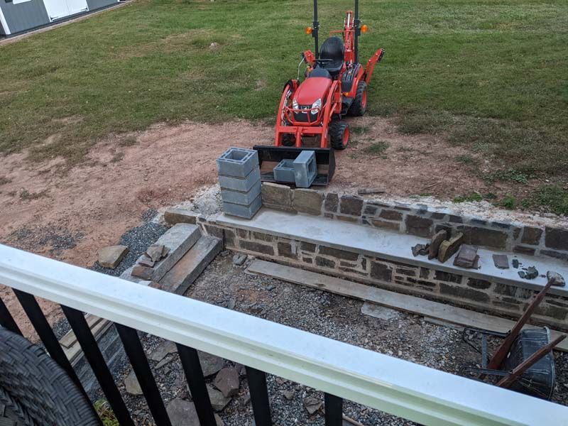 Orange tractor near a construction site with brickwork and concrete blocks.
