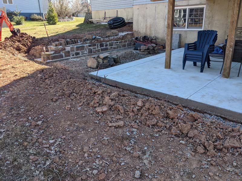 Construction site with a concrete patio, retaining wall, and exposed dirt.