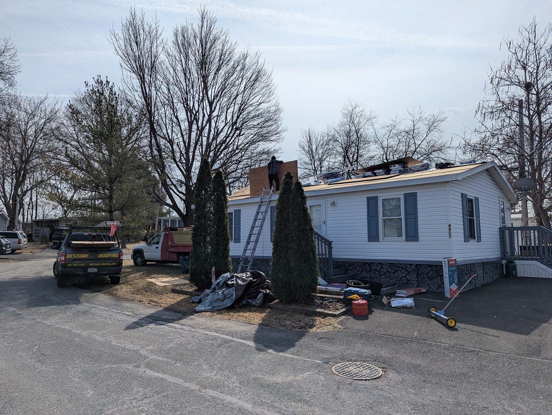 Mobile home under renovation; workers on the roof, with tools and debris on the ground.