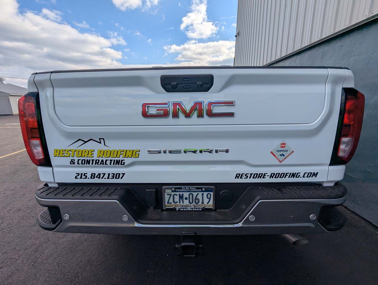 White GMC Sierra truck bed with company logo and license plate, against a cloudy sky.