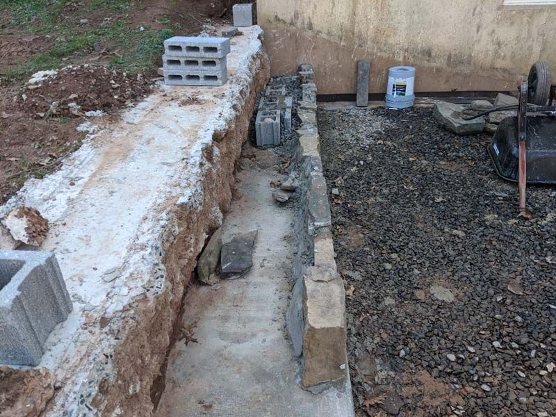 Construction site with concrete foundation being built; blocks, rubble, and tools present.