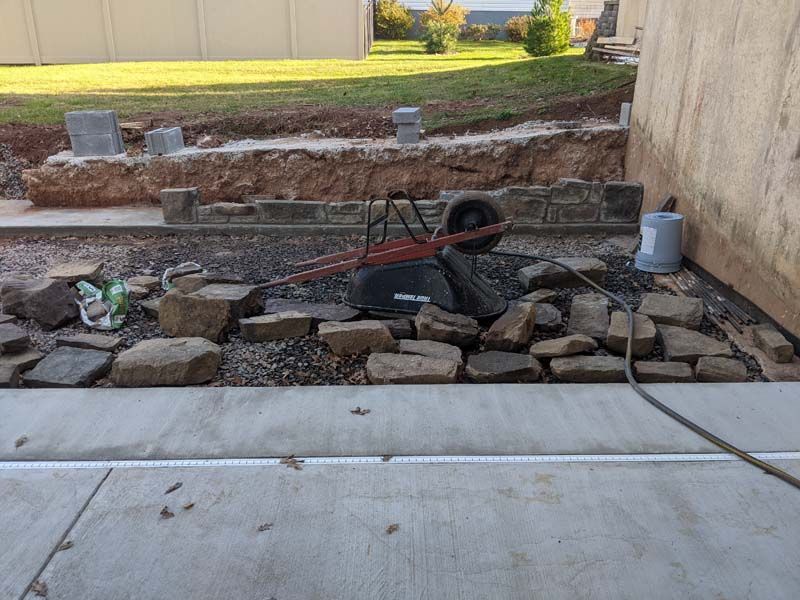 Backyard construction scene: retaining wall under construction with wheelbarrow, rocks, and blocks.