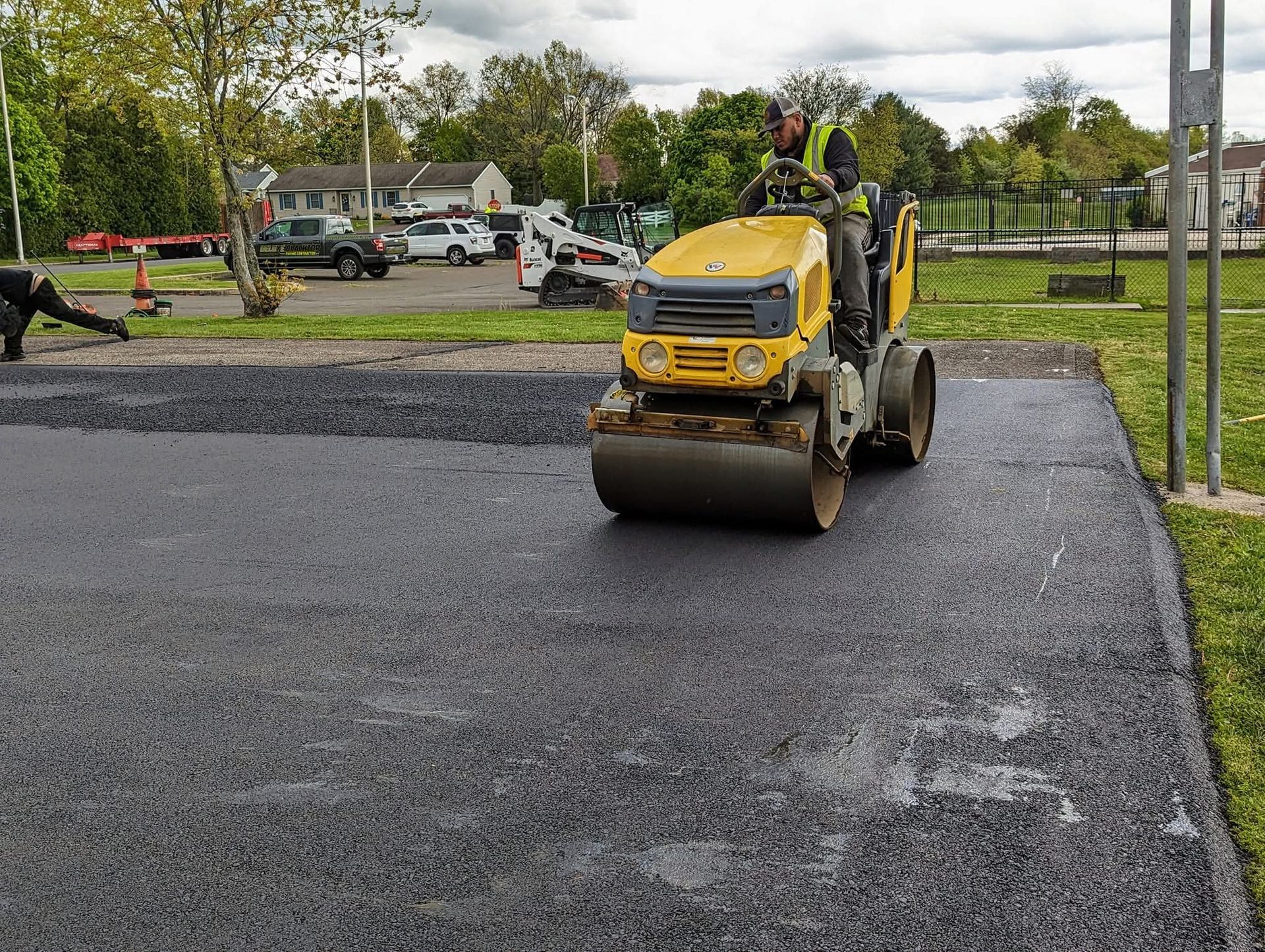Yellow asphalt roller compacts fresh black asphalt in an outdoor setting.