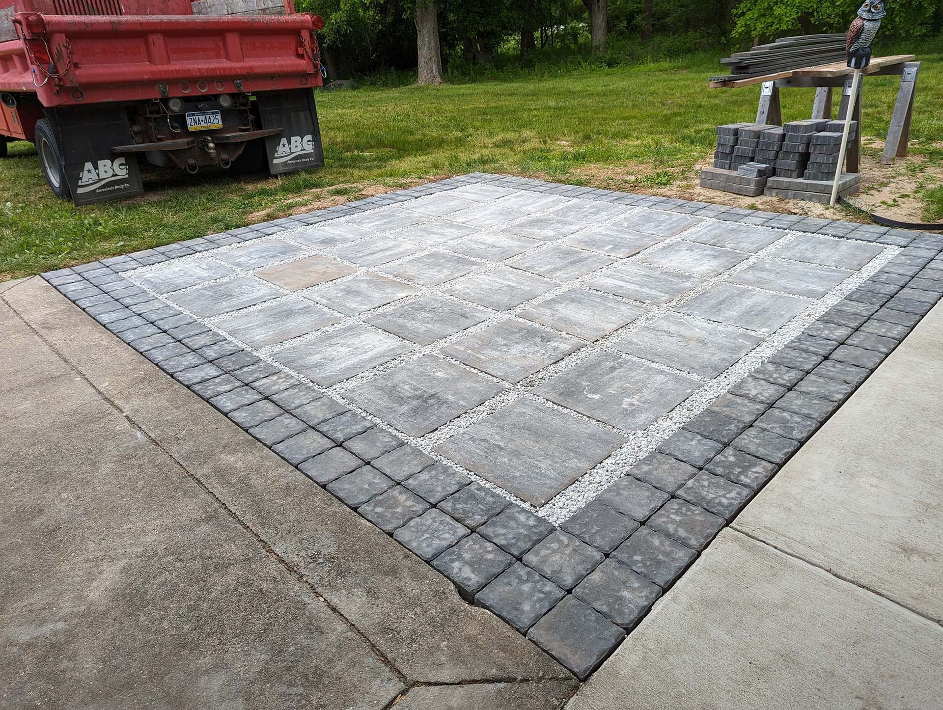 Square stone patio with brick border next to concrete driveway and a red truck.