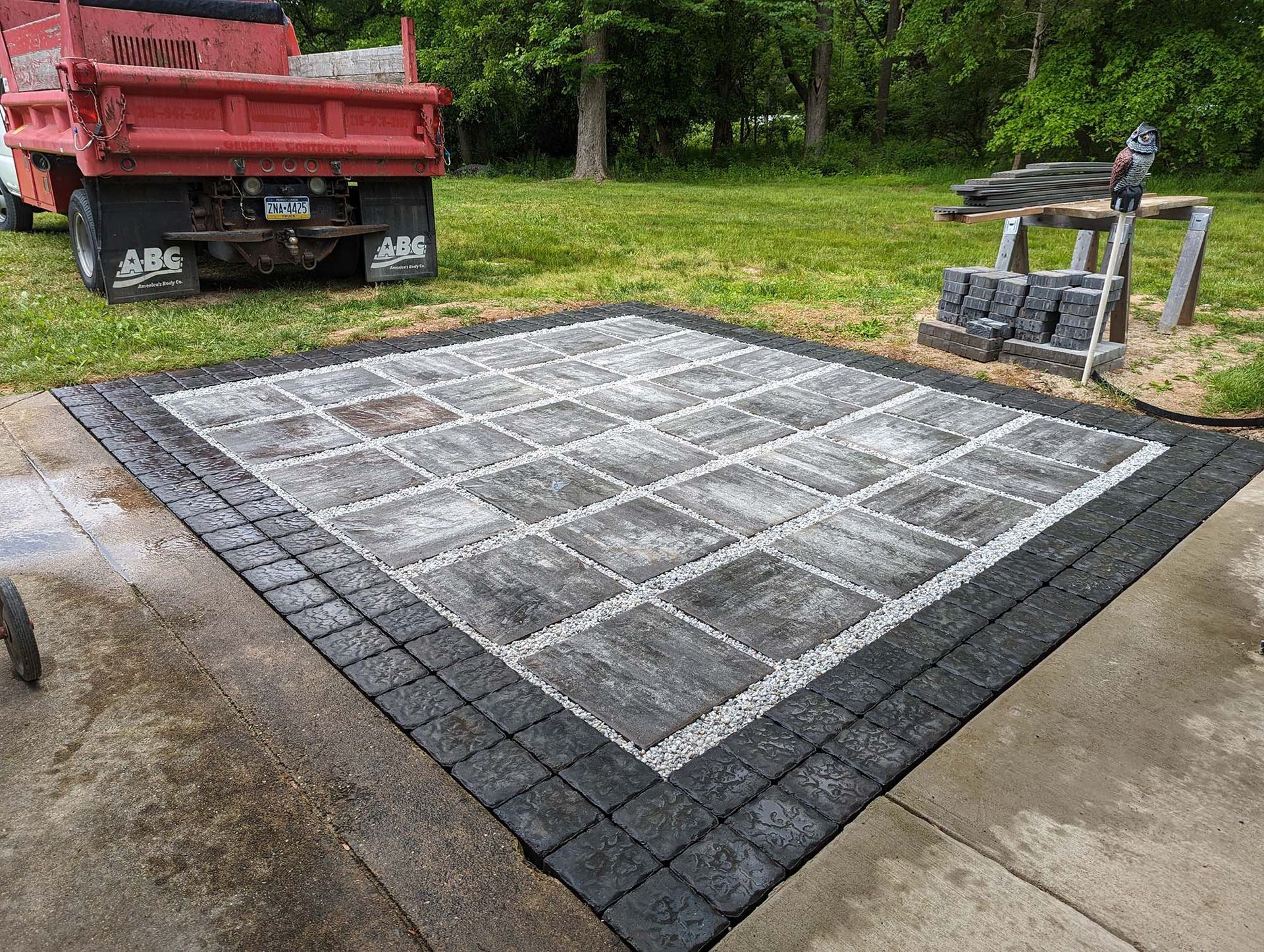 Completed patio with dark border, gray and black pavers, red truck in the background.