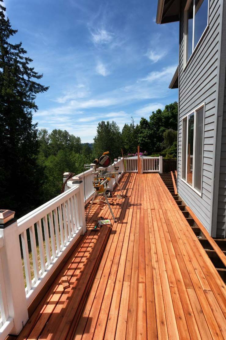Wooden deck attached to a gray house, with white railing and sunny sky.