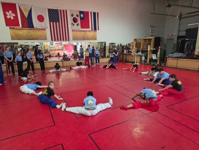 Martial arts class stretching on red mats in a gym with flags on the wall