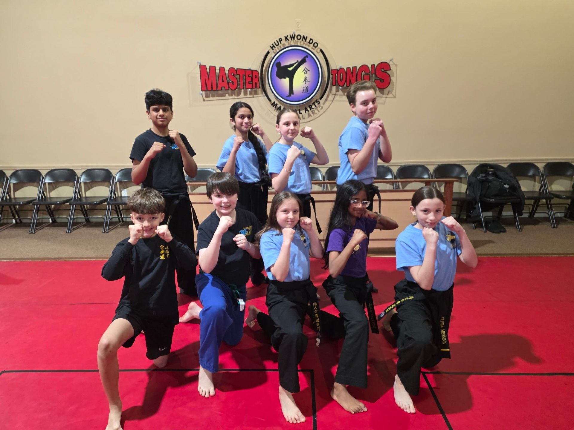 Group of martial arts students posing on a red mat in front of a Master Kim's studio sign.