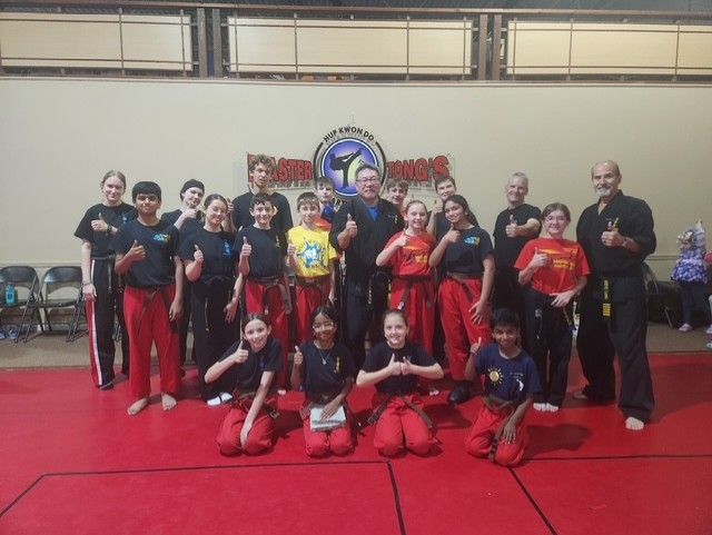 Group of people in red and black costumes posing on a red floor at an indoor event.