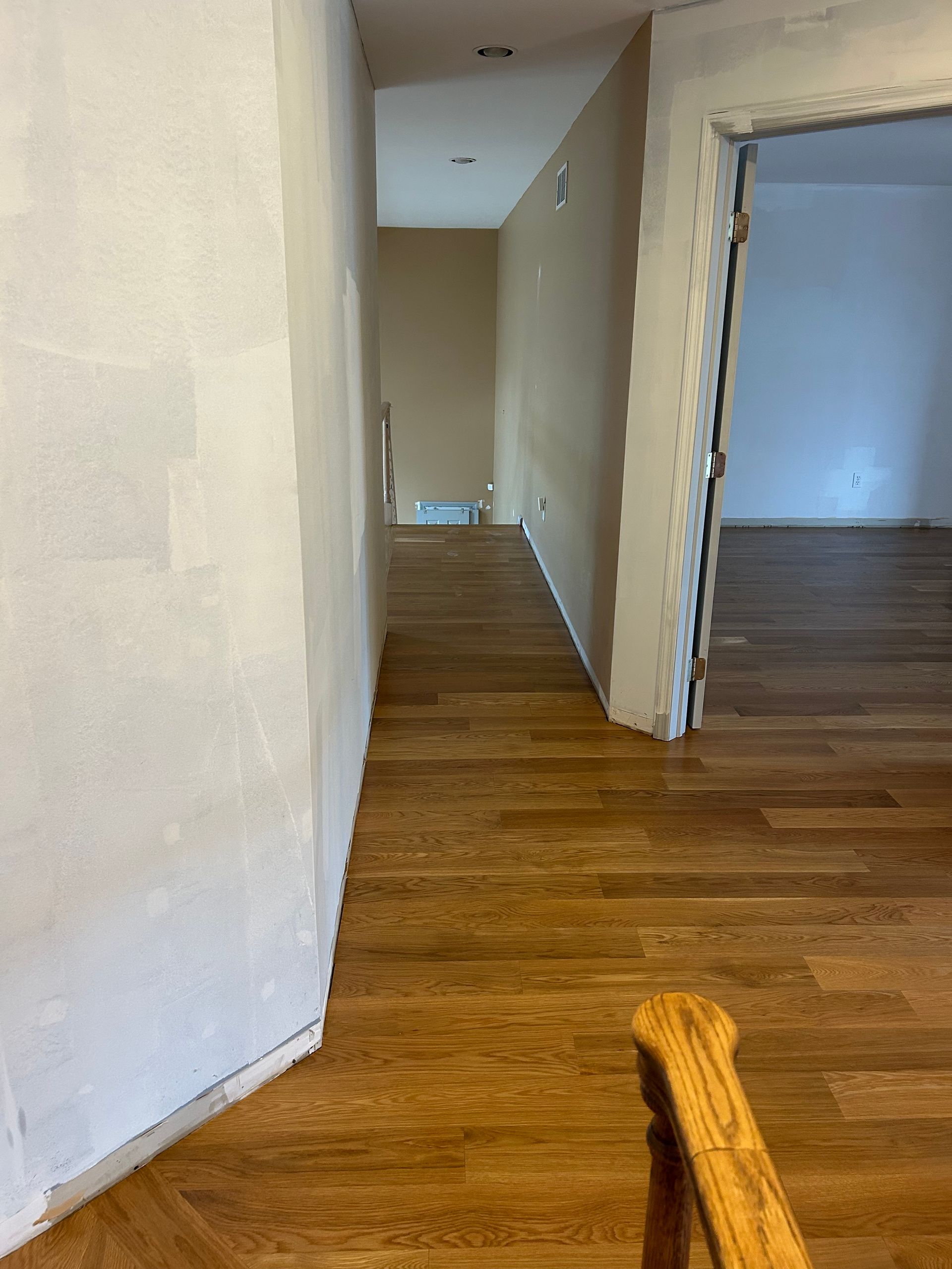 Narrow hallway with white walls and hardwood floors, leading to an open room on the right.