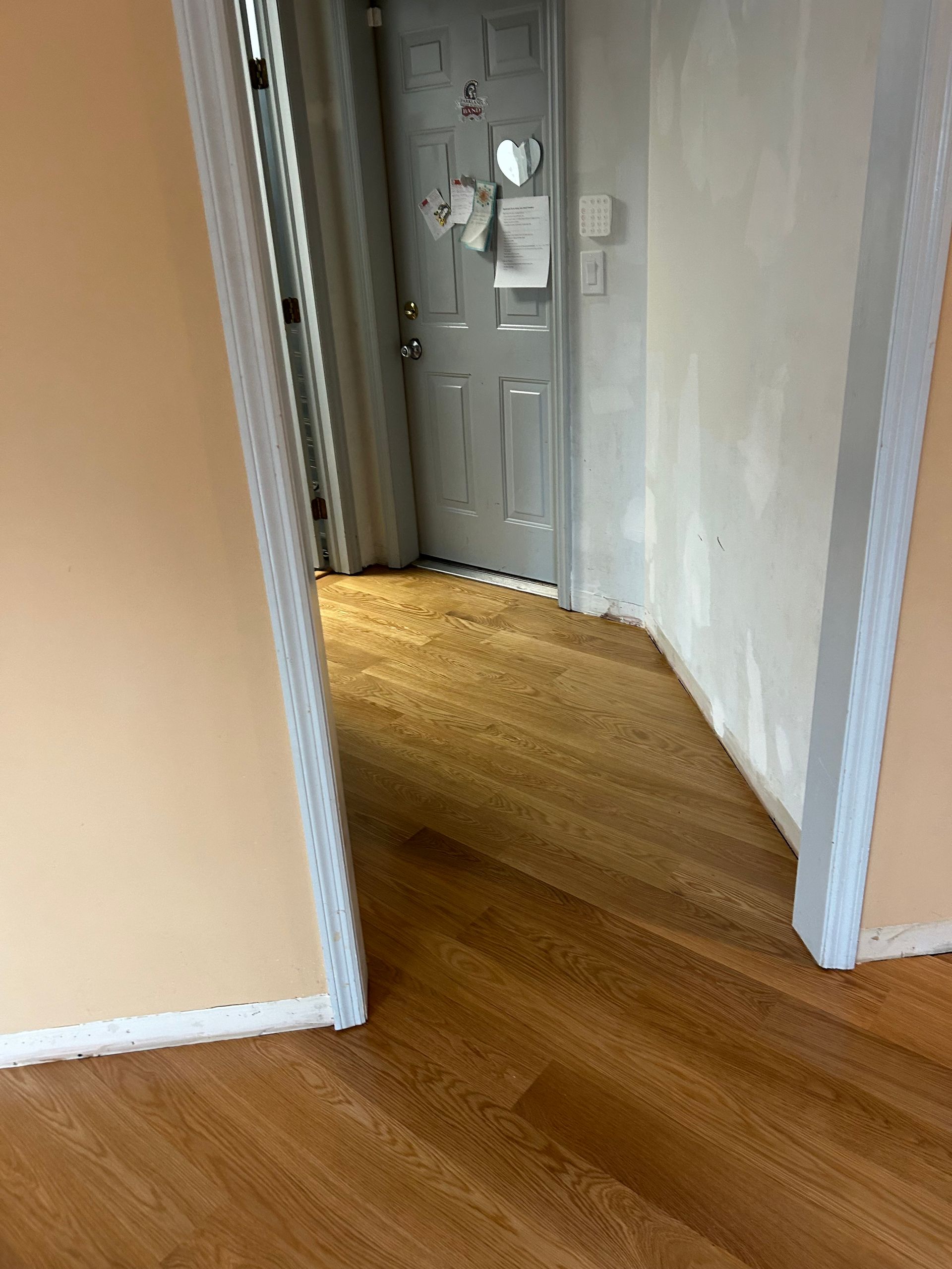 Empty hallway with tan walls, hardwood floors, and a gray door at the end