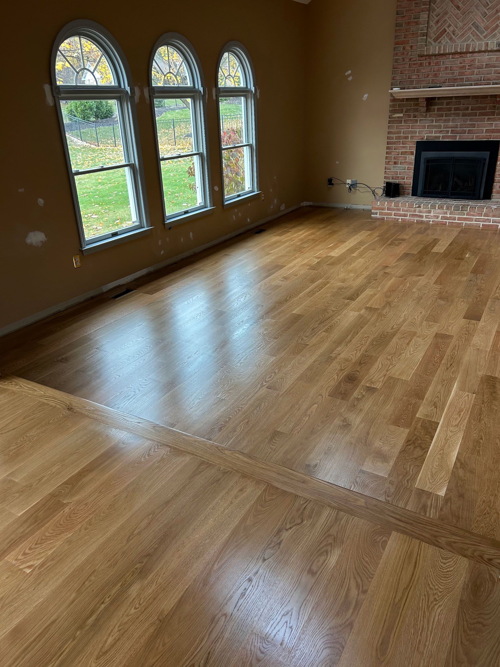Empty living room with glossy hardwood floors, arched windows, and a fireplace