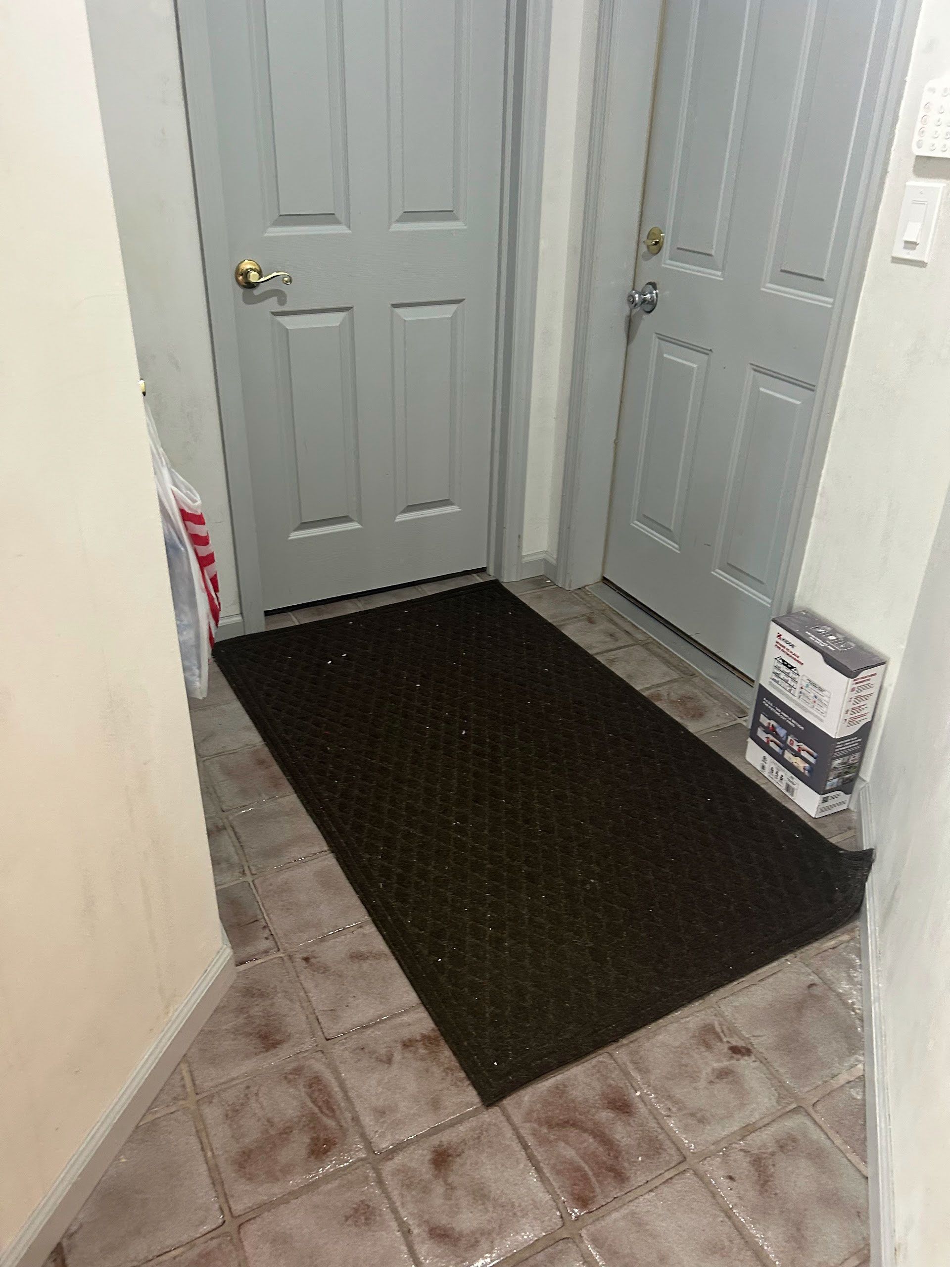 Narrow entryway with white doors, beige tile floor, and a dark rectangular rug