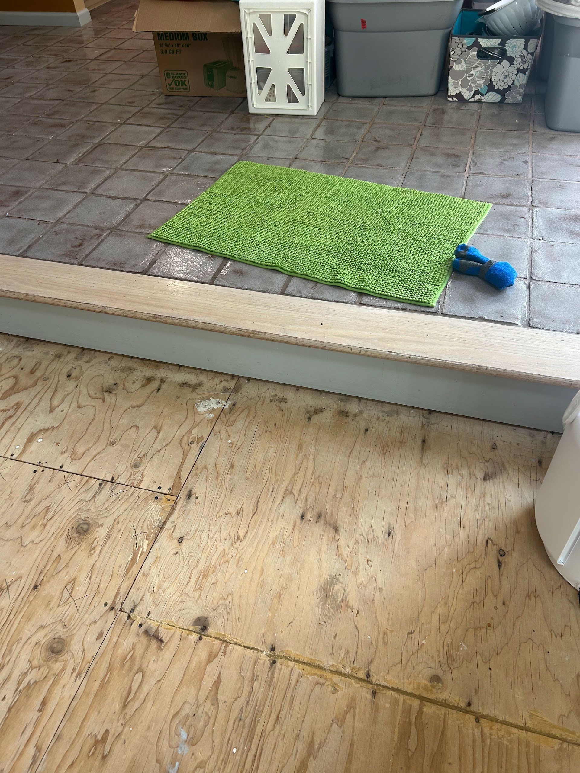 Green mat on a patio step with a blue shoe beside it, leading to a tiled outdoor area.