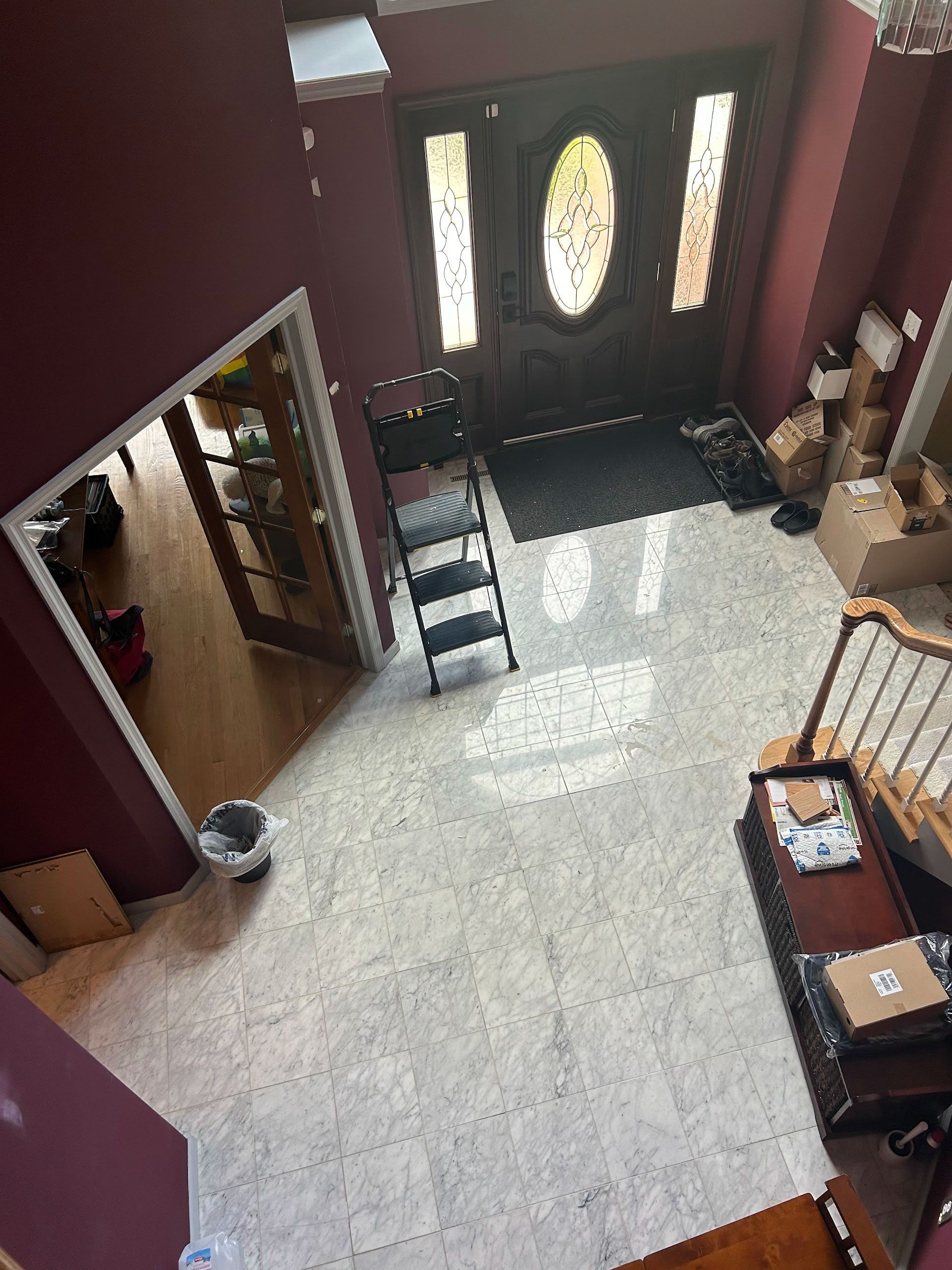 Entryway with maroon walls, tiled floor, front door, and staircase railing in a sunlit home interior