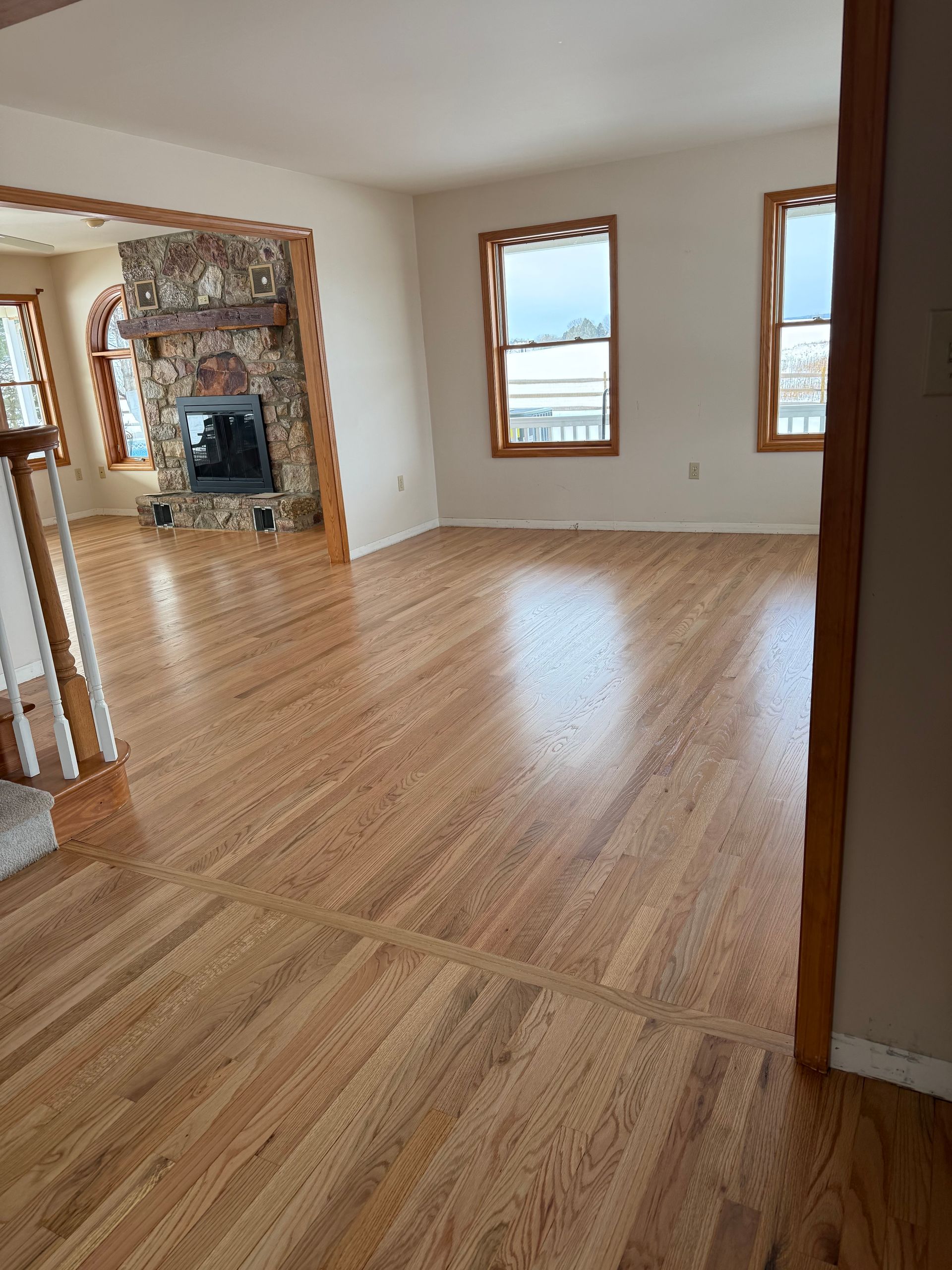 Empty hardwood living room with windows and a mirrored fireplace mantle