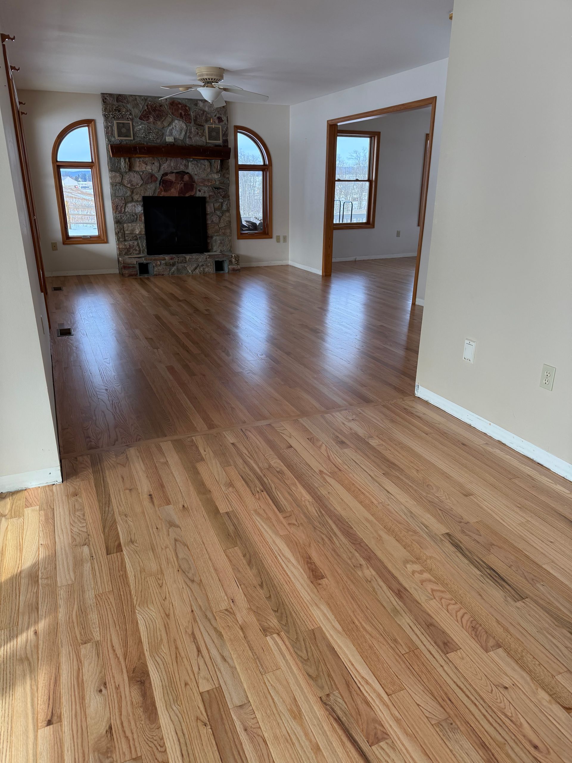 Empty living room with hardwood floors, stone fireplace, and arched windows