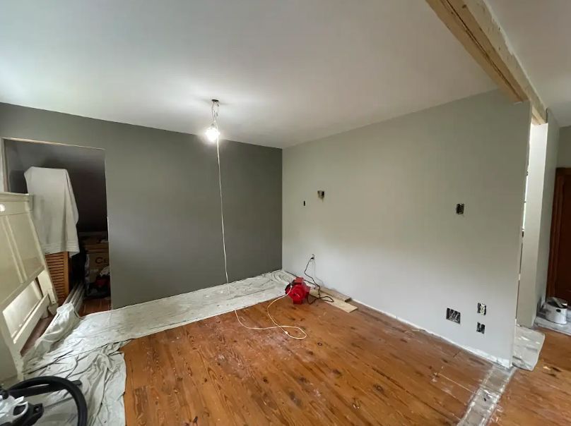 Room renovation with gray and white walls, exposed wood floor, and overhead light.