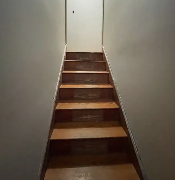 Wooden staircase against gray walls, leading to a closed doorway.