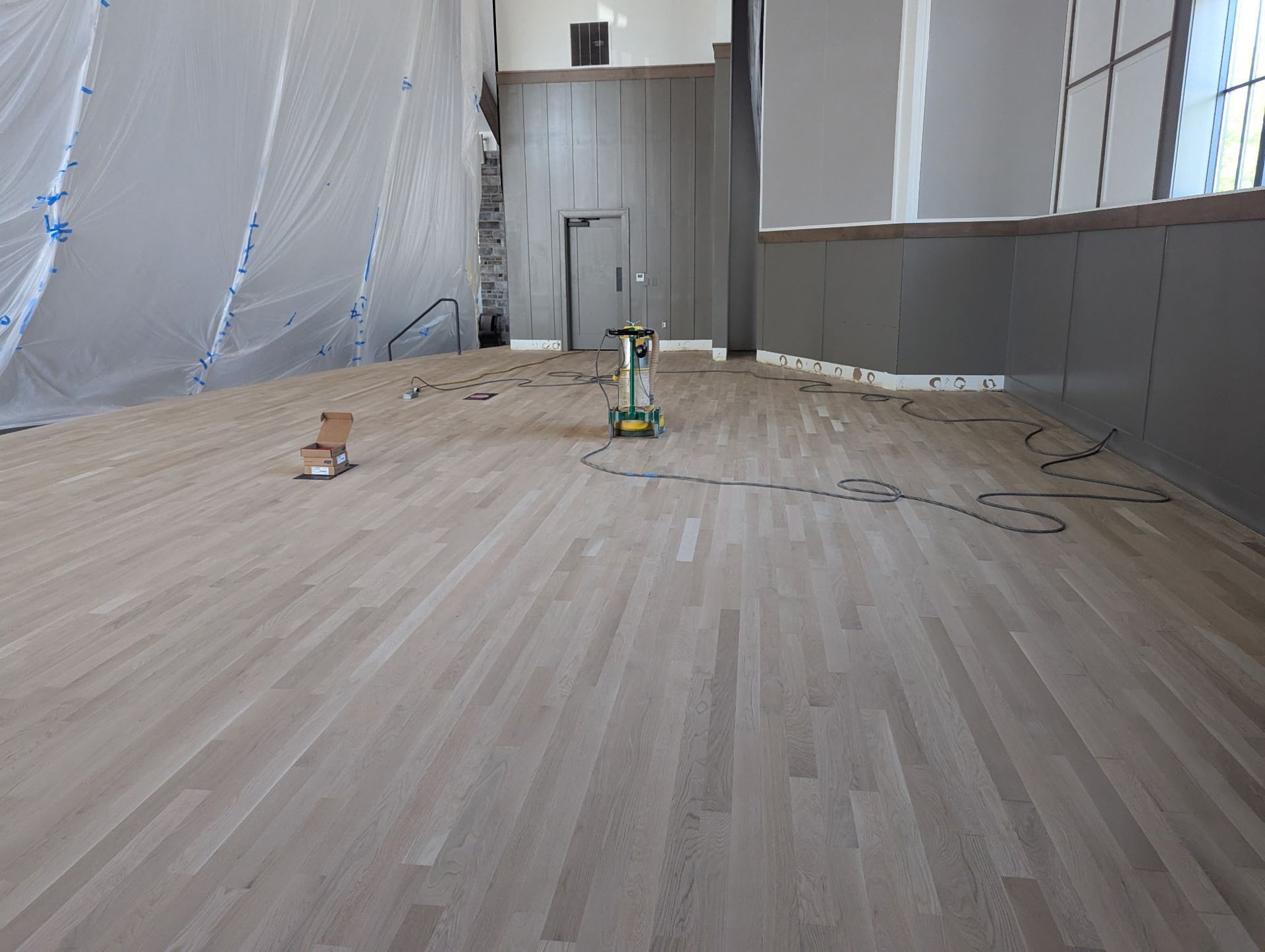 Newly refinished wooden floor in a room being renovated, with tools and protective sheeting.