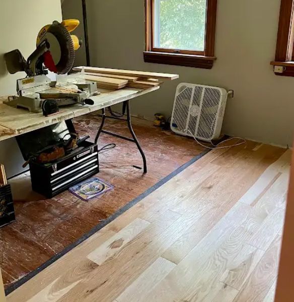 Room with a miter saw, tools, and newly installed light wood flooring next to a darker existing floor.