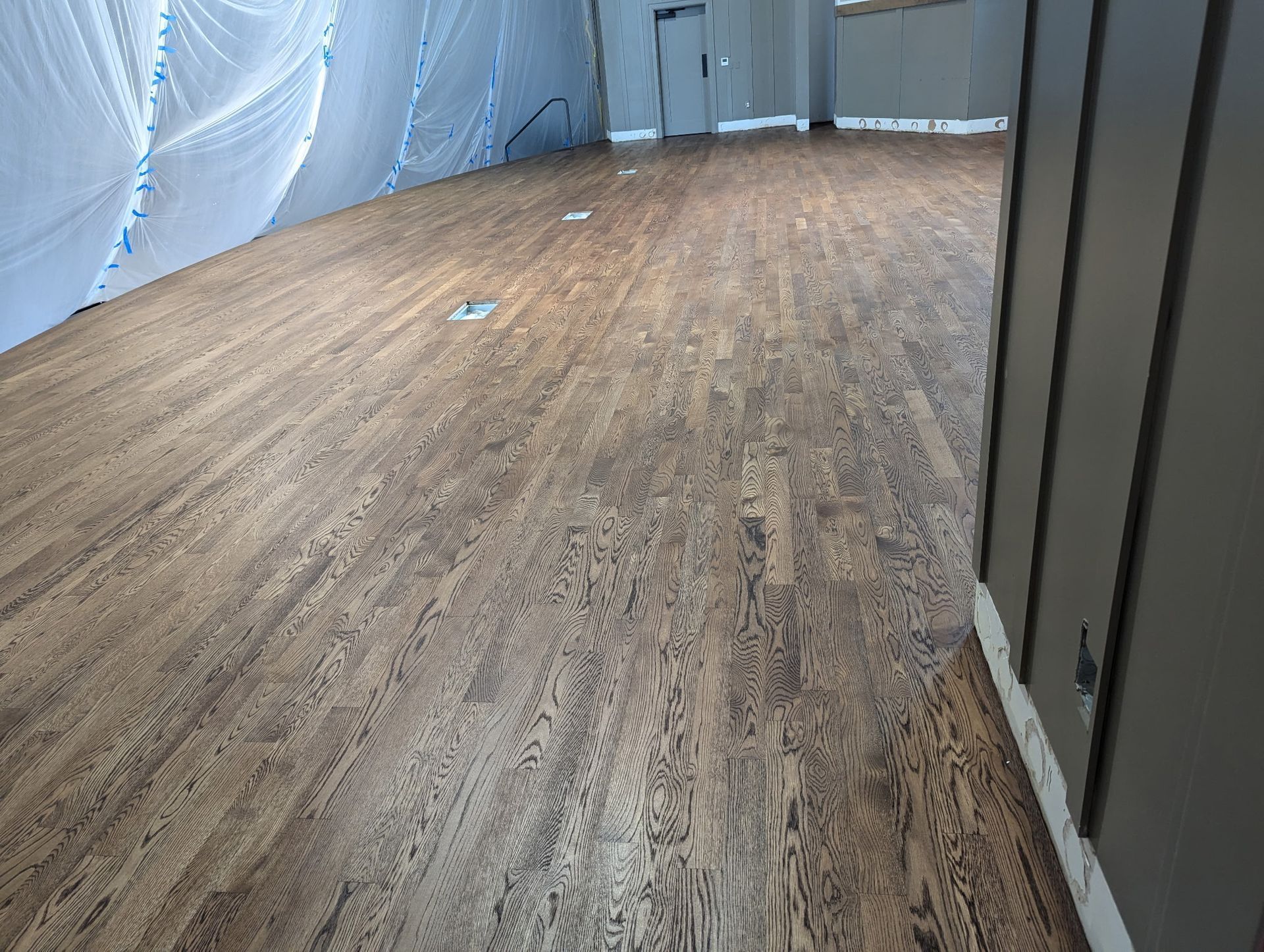 Brown flooring in a room with protective sheeting and dark gray trim.