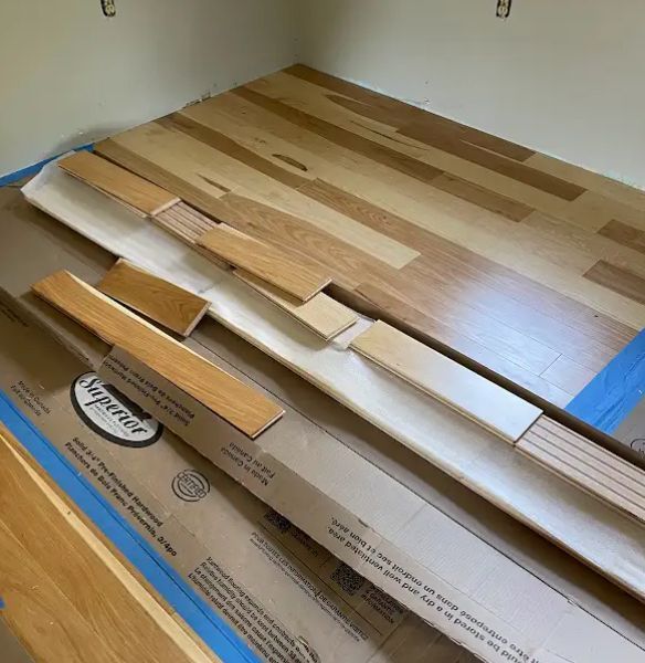 New hardwood flooring installation; wood planks and cardboard box inside a room.