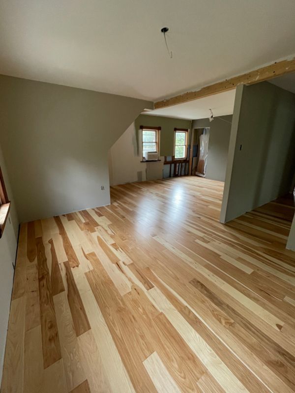 Light wood floor in a room with light gray walls, window, and doorway to another room.