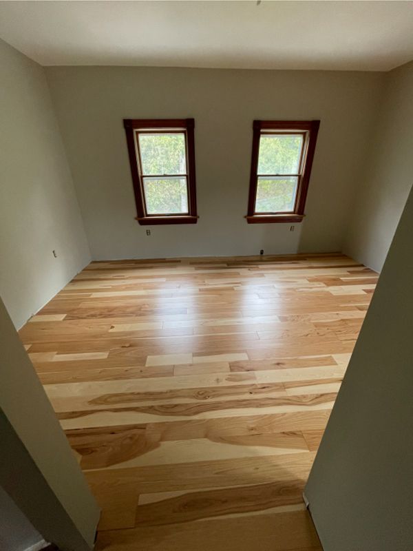 Empty room with wood floors and two small windows with brown frames.