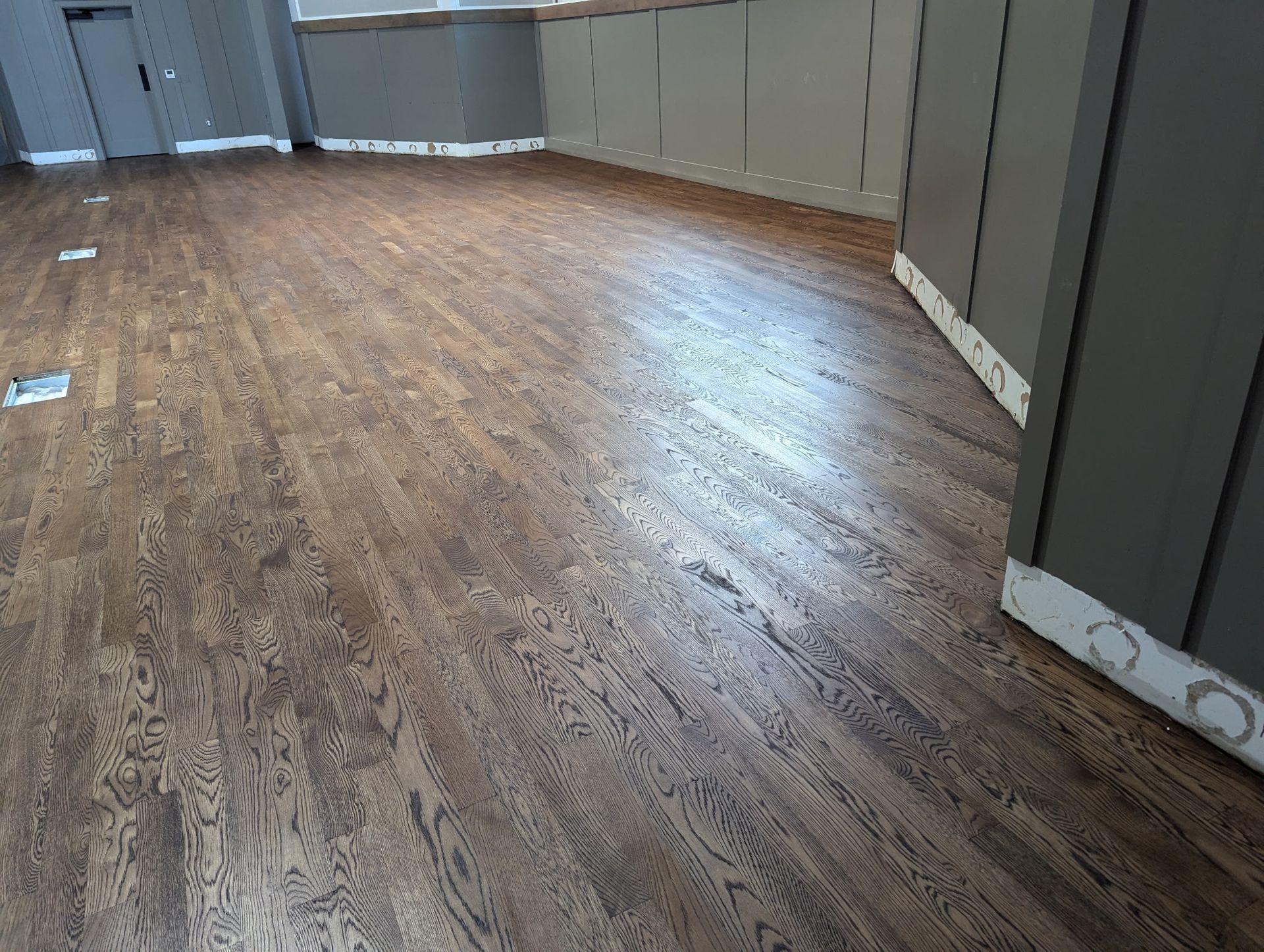 Dark brown wooden floor in a room with gray walls and white trim.