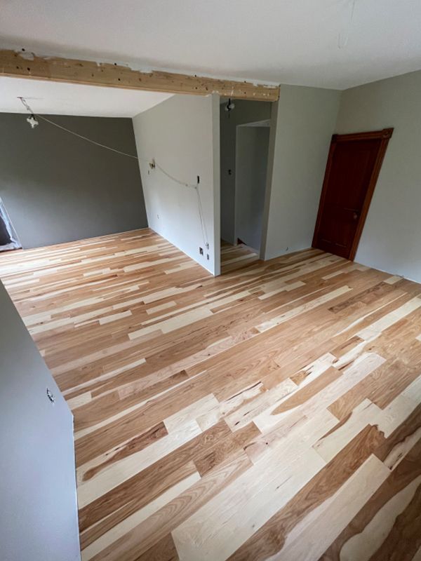 Newly installed wood plank flooring in a room with light gray walls, an open doorway, and a brown door.
