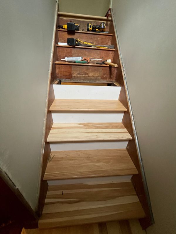 Wooden stairs being remodeled. Some treads are finished, others awaiting installation. Tools rest on unfinished steps.