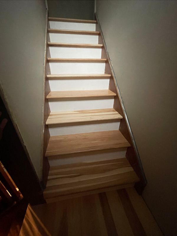 Wooden staircase with white risers and light brown treads, ascending between gray walls.