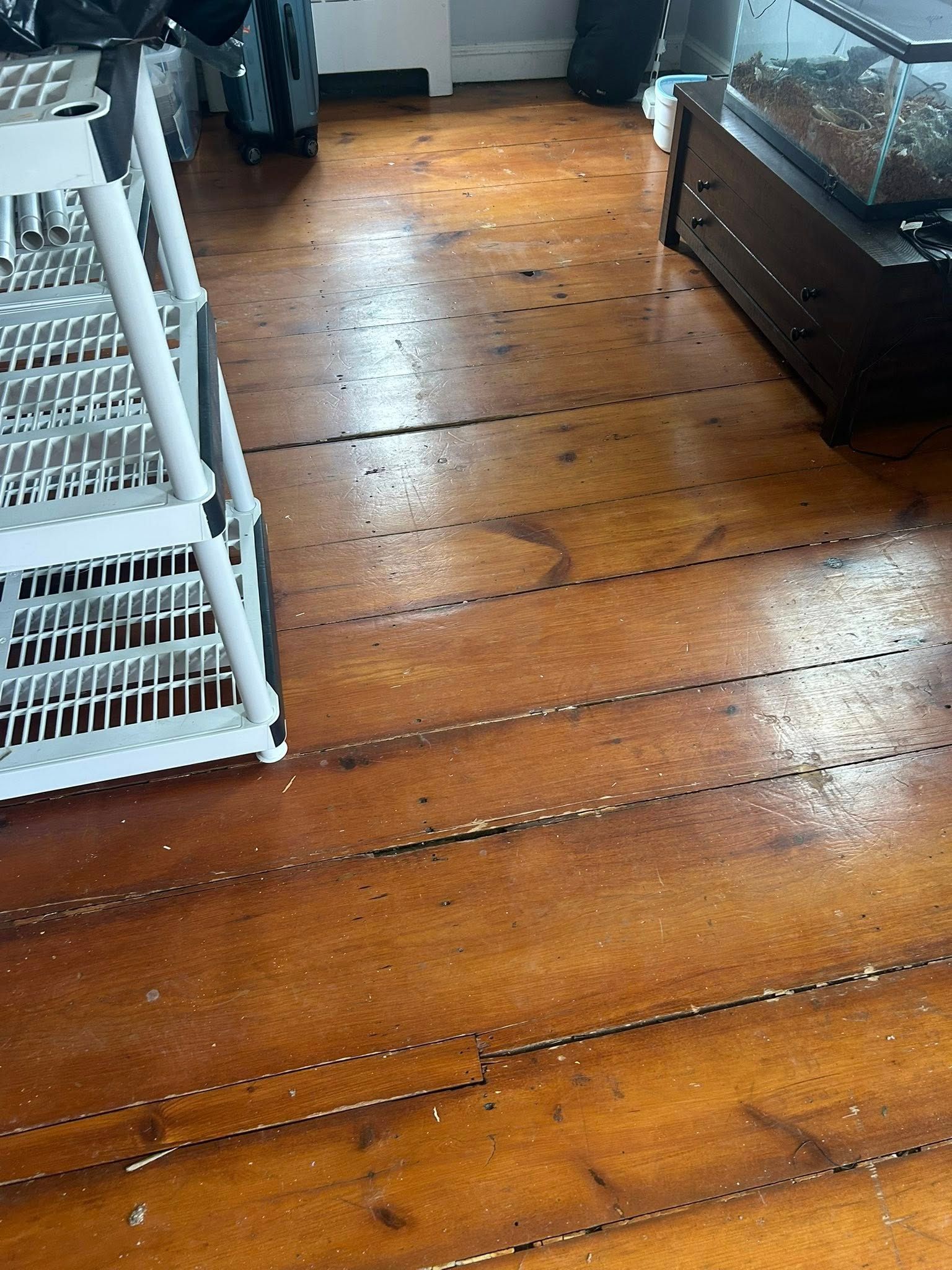 Rustic wooden floor in a room with stacked white wicker baskets and a dark cabinet.