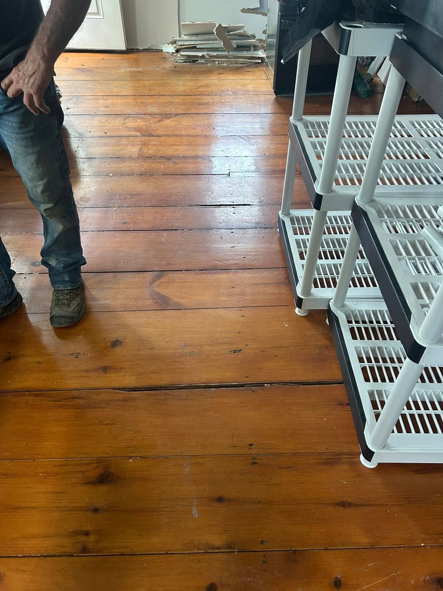 Two people standing on a wooden floor beside white shelving units and a metal cart