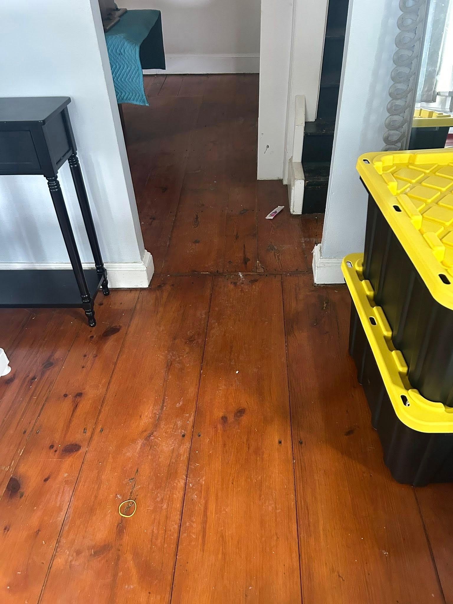 Wooden floor in a narrow hallway with a yellow storage bin, black cart, and doorway ahead.
