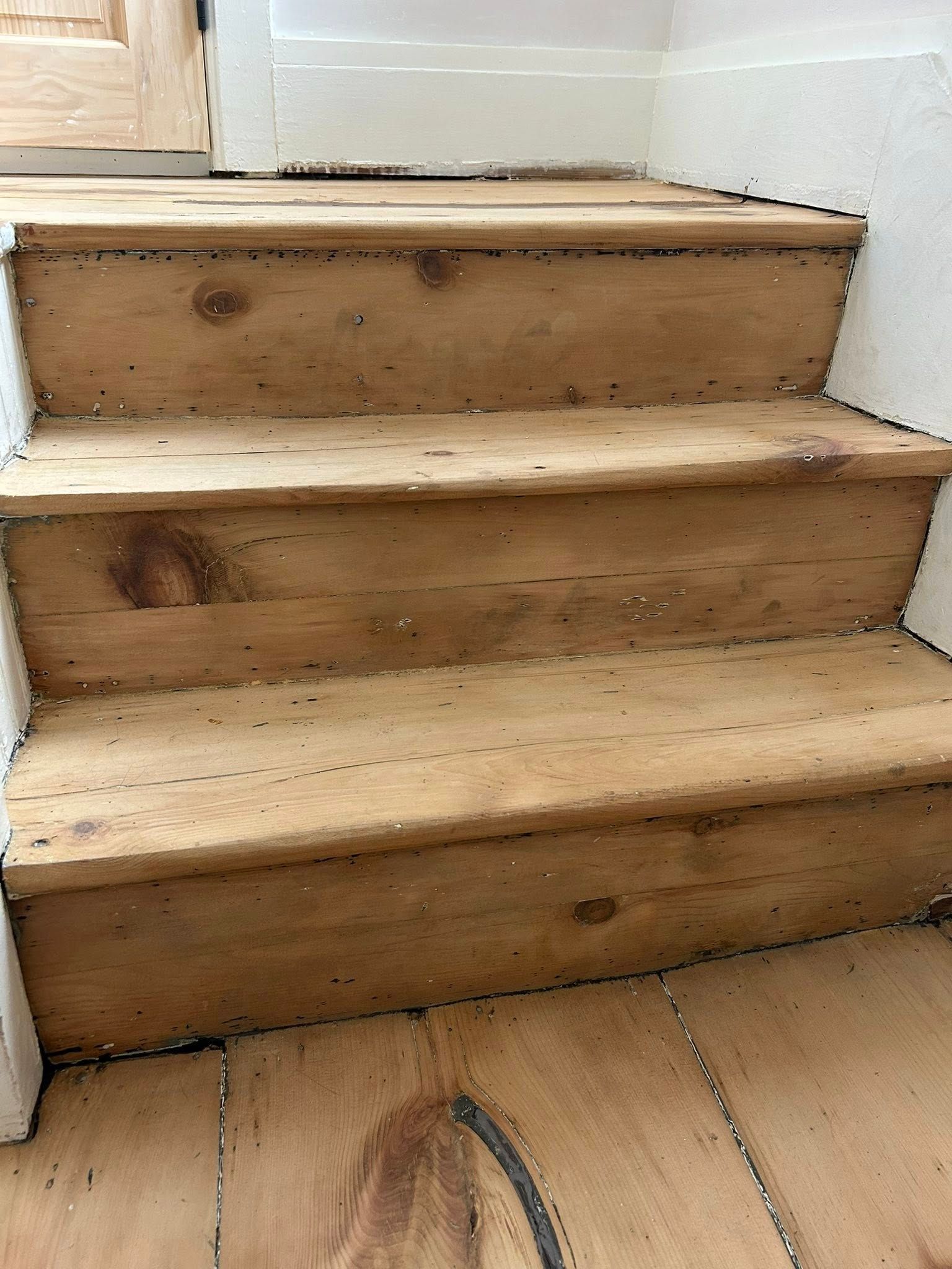 Wooden stairs with worn treads and white-painted side walls, leading up indoors.