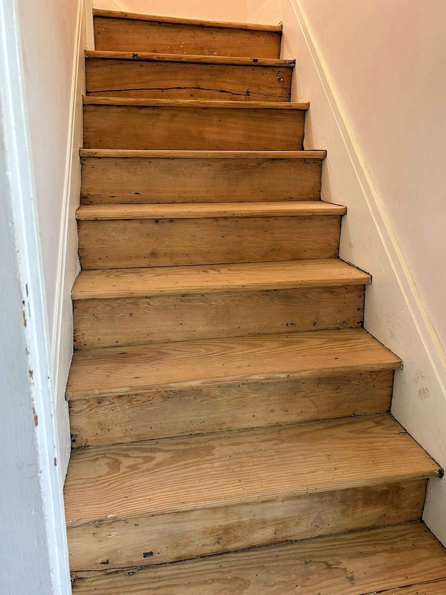 Narrow carpeted staircase with worn wooden steps in a beige hallway